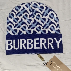 Blå Burberry Mössa - Trendig Burberry mössa med klassiskt mönster och logotyp, perfekt för att hålla stilen varm.