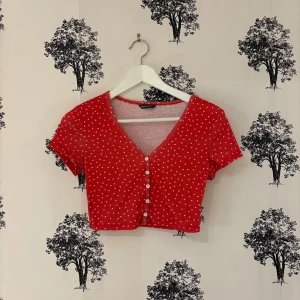 Röd croppad topp med hjärtan från SHEIN - Supergullig röd croppad topp från SHEIN med små vita hjärtan över hela. Toppen har v-ringning, korta ärmar och knappar framtill. Perfekt för dig som vill ha en söt och trendig look.