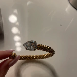 Caroline Svedbom, classic rope 1295 kr riktigt pris  - Unikt guldfärgat armband med pärlstruktur och en stor, droppformad klar kristall framtill. Armbandet är öppet och har fina detaljer i ändarna. Perfekt för dig som vill sticka ut med ett statement-smycke.
