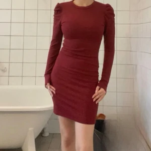 Vinröd tight klänning med puffärmar från nakd  - Vinröd, figurnära klänning med långa puffärmar och rund halsringning. Kort modell som sitter snyggt på kroppen och har en stilren, enkel design utan mönster. Passar perfekt till julavslutningen som kommer snart. Den är använd men den har inga permanenta fläckar (har inga fläckar alls), och materialet är fortfarande fin. Har två.