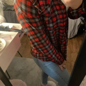 Röd rutig skjorta från Size Needle XS - Snygg röd och svart rutig skjorta från Size Needle i storlek XS. Skjortan har klassisk krage, knäppning framtill och långa ärmar med manschett. Perfekt för dig som gillar en avslappnad men ändå trendig stil.