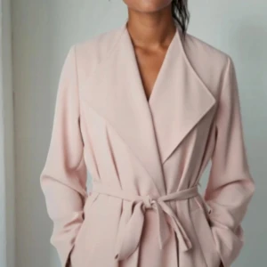 Ljusrosa trenchcoat från Lindex, stl S, nyskick! - Säljer en ljusrosa trenchcoat från Lindex i storlek S. Jackan har breda slag, knytbälte i midjan och långa ärmar. Stilren och enkel design som ger en snygg siluett. Perfekt för dig som gillar klassiska och feminina plagg.