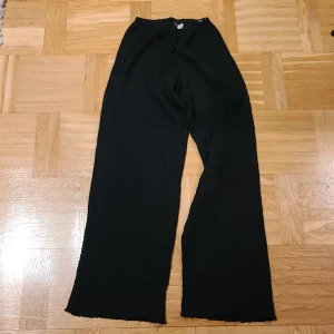 Svarta wide byxor från Divided XS - Svarta byxor från Divided i storlek XS med breda ben och elastisk midja. Materialet är ribbat och har en skön, mjuk känsla. Perfekt för dig som gillar en avslappnad och trendig look med lite extra volym i benen.