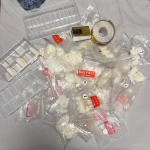 Stort kit med lösnaglar och nagelformar - Säljer ett stort kit med mängder av lösnaglar i olika storlekar och former, både i genomskinligt och mjölkvitt material. Flera plastaskar och påsar med 50-pack, samt guldfärgade nagelformar på rulle. Perfekt för dig som älskar att fixa naglarna hemma.