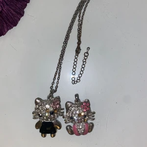 Glittriga Hello Kitty halsband - Ett söt hello kitty halsband och en  berlock, dekorerade med glittrande stenar i silver. En sten har trillat av på båda, man kan se de på bilden!💕🌸