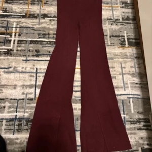 Mörkröda ribbade bootcut byxor - Snygga mörkröda ribbade byxor med bootcut-ben och hög midja. Materialet är mjukt och stretchigt, vilket gör dem riktigt sköna att bära. Perfekta för dig som gillar en trendig och avslappnad look med lite extra attityd.