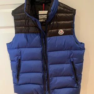Blå och svart dunväst från Moncler - Fräsch blå/svart Moncler väst i storlek M med lite mer utstickande färger. Skulle säga att den passar både M och L. Bra tjocklek så den är användbar även på vintern. Skicket är bra inte så överdrivet använd. Som alltid kan priset diskuteras!