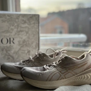 Beige Asics sneakers med mesh - Säljer ett par snygga Asics sneakers i beige med klassisk logga på sidan. Skorna har mesh-ovandel för extra andningsförmåga och en riktigt bekväm sula. Perfekta för dig som gillar stilrena och sportiga skor med snörning och rund tå.