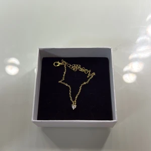 Guldigt armband med hjärtberlock - Fint armband i guldtonad kedja med en liten hjärtformad berlock som glittrar. Perfekt för dig som gillar enkla men söta smycken. Justerbar längd med karbinlås. Kommer i ask.