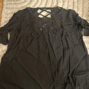 Svart spetsklänning från Zara Basic - Svart kortklänning från Zara Basic med vacker spets upptill och snörningsdetalj i ryggen. Klänningen har korta ärmar och en luftig passform. Perfekt för dig som gillar stilrena och feminina detaljer.