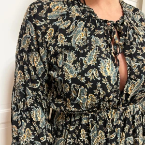 Svart blommig kortklänning från Zara - Supersöt svart kortklänning från Zara med blommigt mönster i grönt, beige och gult. Klänningen har långa ärmar, knytning vid halsen och volangdetaljer i kjolen. Perfekt flowy passform och lätt material som känns luftigt.