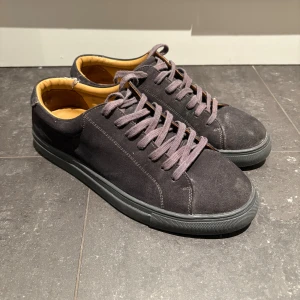 Mörkgrå mockasneakers från Myrqvist - Snygga mörkgrå sneakers från Myrqvist i mocka med matchande grå snörning och svart sula. Skorna har en klassisk låg profil och insida i ljusbrunt läder för extra komfort. Perfekta för dig som gillar stilrena och tidlösa sneakers.