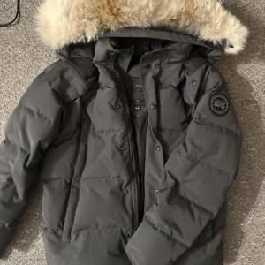Grå Canada Goose dunjacka med päls - Säljer en grå dunjacka från Canada Goose med fluffig päls på huvan och klassisk patch på ärmen. Jackan har långa ärmar, dragkedja och knappar framtill samt flera fickor. Perfekt för kalla vinterdagar och har en riktigt snygg, oversized look. Äkta jacka perfekt skicka nytt skick 
