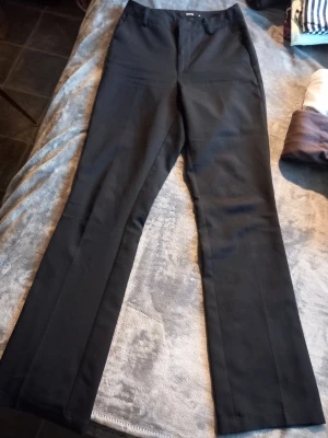 Svarta kostymbyxor från Bik Bok - Svarta kostymbyxor från Bik Bok i klassisk rak modell. Byxorna har en stilren look och är gjorda i ett mjukt material som känns skönt mot huden. Perfekta för dig som gillar enkel och clean stil.