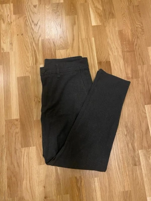 Mörkgrå kostymbyxor Zara - Snygga mörkgrå kostymbyxor med diskret rutigt mönster i strl 42 från Zara . Byxorna har raka ben, bälteshällor och knäppning fram. Två fickor bak med knapp och två sidofickor. 