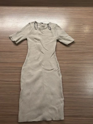 Beige ribbad långklänning - Säljer en beige ribbad långklänning med korta ärmar och rund hals. Klänningen har en kroppsnära passform och är tillverkad i ett mjukt stickat material som ger en skön känsla. Perfekt för dig som gillar minimalistisk och stilren look. Har ingen lapp men är från H&M