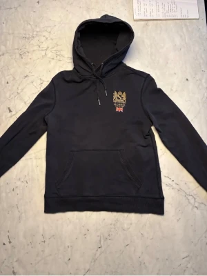 Blå hoodie från morris  - Snygg blå hoodie från morris med det klassiska morris märket broderat på bröstet. Tröjan kostar cirka 1500kr ny och är i fint skick 