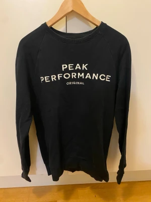 Svart sweatshirt från Peak Performance - Säljer en svart sweatshirt från Peak Performance med vit broderad logga på bröstet i strl M. Tröjan har rund halsringning, långa ärmar och ribbade muddar.