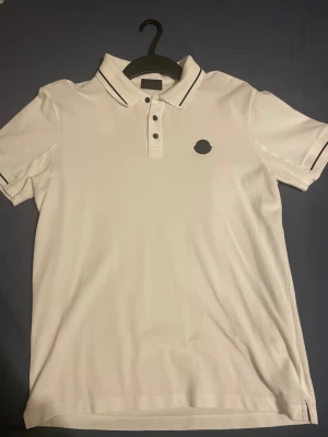 Moncler - Vit pikétröja från Moncler med svart logotyp på bröstet och svarta detaljer på krage och ärmslut. Endast använd ett fåtal gånger. Alla og tags följer med! Bara att höra av er vid funderingar! Mvh
