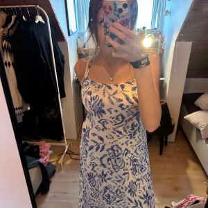 Blommig blå vit sommar långklänning med smala axelband - korad knytning i rygg. Säljer en superfin långklänning med smala axelband och blått blommigt mönster på vit botten. Klänningen har en rak och figurnära passform som ger en snygg siluett. Perfekt för dig som gillar romantiska och somriga vibes.