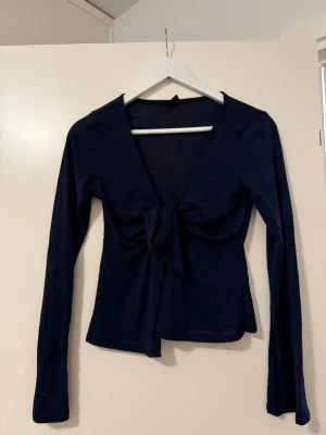 Marinblå långärmad topp med knytning - Marinblå topp med långa ärmar och djup v-ringning. Framtill finns en knyt-detalj.