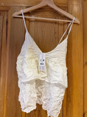 Vit omlott linnetopp med volanger - Säljer en vit linnetopp från Ginatricot i storlek S. Toppen har tunna axelband, omlott-design och är dekorerad med volanger och ett krinklat tyg som ger en cool struktur. Perfekt för sommarens alla häng och outfits. Aldrig använd då den tyvärr var för stor för mig💘 Pris går att diskutera🙌🏼