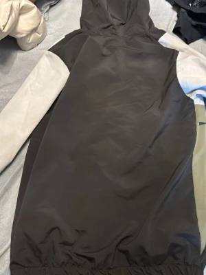 Lacoste vindjacka med huva - Säljer en snygg colorblock vindjacka från Lacoste med huva. Jackan har dragkedja framtill, två fickor med dragkedja och coola färgblock i svart, vitt och olivgrönt. Perfekt för dig som vill ha en stilren och sportig look.