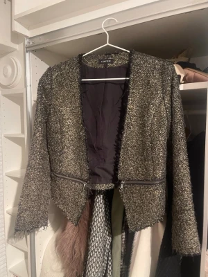 Svart och guld kavaj från Lindex - Snygg kavaj från Lindex i svart och guld med grov textur och råa kanter. Jackan har lång ärm, dragkedjedetaljer framtill och är fodrad med svart tyg. Perfekt för dig som gillar en edgy och unik stil.