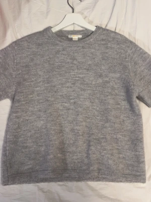 Grå stickad tröja från Gina Tricot - Mysig grå stickad tröja från Gina Tricot i storlek 158/164. Tröjan har en rund halsringning och är kortärmad. Perfekt för kyliga dagar och enkel att matcha med jeans eller kjol.