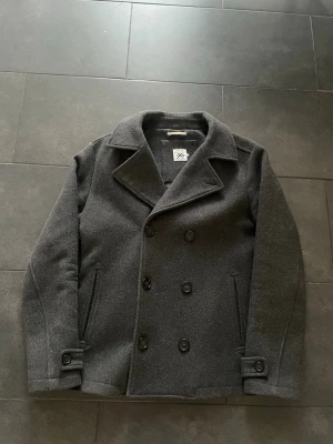 Mörkgrå skepparkavaj i ull - Klassisk mörkgrå skepparkavaj från pier one i ullmix. Dubbelknäppt med sex knappar framtill, bred krage och två snedställda fickor. Snygga detaljer vid ärmslut och rak passform. Perfekt för kyliga dagar.