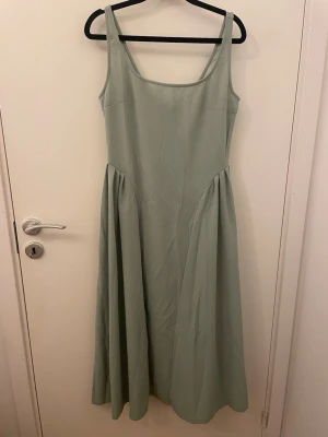 Ljusgrön långklänning med dragkedja - Snygg ljusgrön långklänning med breda axelband och rundad urringning. Klänningen har en markerad midja och ett lätt utställt fall. Dragkedja baktill för enkel påklädning. Materialet känns mjukt och har en slät yta.köpt ifrån Cider. 