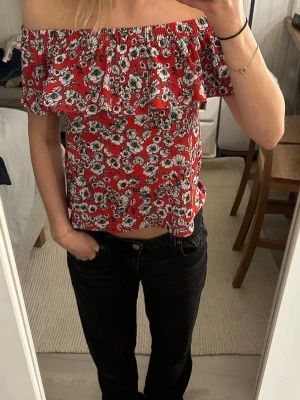  Offshoulder topp - Superfin röd offshoulder topp med vita och svarta blommor. Toppen har volang upptill och resår som gör att den sitter snyggt både på axlarna och offshoulder. Perfekt till sommaren och enkel att styla med jeans eller kjol. Använd fåtal gånger!❤️🌹Skulle säga att den passform för XXS-S🙌