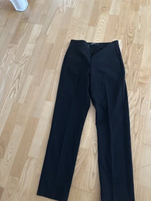 Svarta kostymbyxor Gina Tricot XS - Snygga svarta kostymbyxor från Gina Tricot i storlek XS. Byxorna har raka ben, diskreta fickor bak och stängs med dragkedja och hyska fram. Perfekta till en clean och stilren look. Materialet känns mjukt och följsamt.