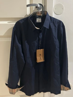 Mörkblå skjorta från Burberry, L - Snygg mörkblå skjorta från Burberry. Sitter som en storlek M. Helt ny och oanvänd. Fraktas inom 48 timmar efter köp🚛