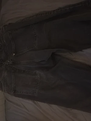 Svarta loose fit jeans från H&M - Svarta jeans från H&M med loose fit och justerbar midja. Klassisk femficksmodell med breda ben och bekväm passform. Perfekta för dig som gillar avslappnad stil och vill ha extra rörelsefrihet. Materialet är jeans och färgen är mörk svart.