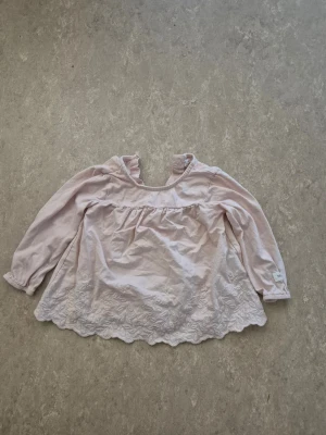 Blus - Säljer en söt ljusrosa blus från Newbie i storlek 74. Blusen har långärmade ärmar med resår, hals med knapp och fina broderade spetsdetaljer längs nederkanten. Perfekt för dig som gillar romantisk och mjuk stil.