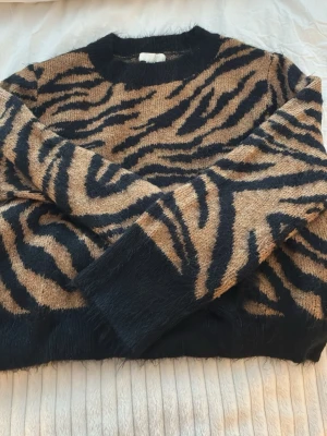 Stickad tröja med zebramönster H&M - Säljer en stickad tröja från H&M i storlek S med fett zebramönster i svart och beige. Tröjan har rund hals, långa ärmar och mjuka muddar. Perfekt för dig som gillar djurmönster och vill ha en mysig och snygg look.