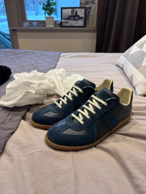 Maison Margiela blå sneakers - Maison Margiela sneakers i marinblå mocka och skinn med vita snören och beige gummisula. Klassisk rund tå och platt sula, snygg retrostil med kontrasterande material. Perfekt för dig som gillar stilrena och unika sneakers.