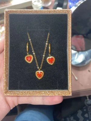 Guldiga öronhängen och halsband  - Ett par guldiga öronhängen med hjärt formad röd sten, och ett halsband som matchar. Lådan ingår också 💕