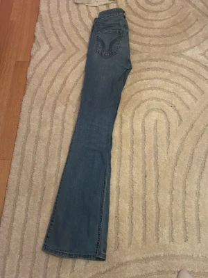 Bootcut jeans från Hollister, midwaist - Säljer ett par ljusblå bootcut jeans från Hollister i modellen Mid-Rise Boot. Klassisk femficksdesign, snygg tvätt och bekväm midwaist. Perfekta till sneakers eller boots för en avslappnad look.