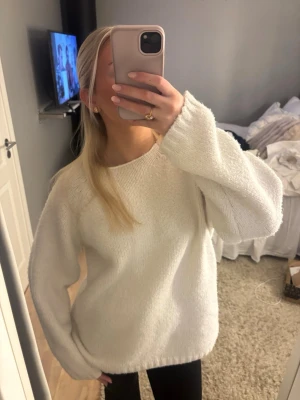 Vit stickad oversized tröja - Mysig vit stickad tröja med rund hals och långa ärmar. Tröjan har en oversized passform och är gjord i ett mjukt, fluffigt material som känns riktigt skönt mot huden. Perfekt att slänga på sig när det är kallt ute.