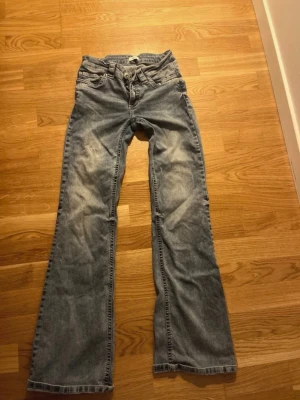 Bootcut jeans från Nelly, blå denim - Snygga blå bootcut jeans från Nelly med klassisk femficksdesign och knappar på bakfickorna. Jeansen har en låg midja och är tillverkade i mjukt denim-material. Enkelt och styla till