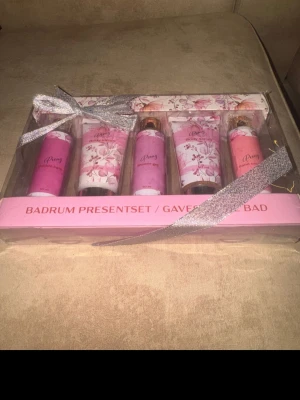 Peony badrum presentset rosa - Presentset med Peony badprodukter i rosa och vita förpackningar med blommigt mönster. Innehåller bubble bath, body lotion, shower gel, body scrub och hand cream, alla i 50 ml tuber och flaskor. Snyggt inslaget med silvrigt band, perfekt som gåva.