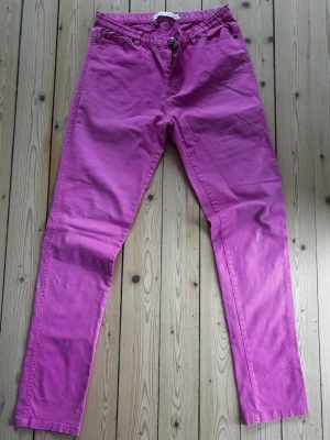 Rosa jeans från Uniq - Säljer ett par snygga rosa jeans från Uniq  i storlek 32. Byxorna har klassisk femficksdesign, knapp och dragkedja i gylfen samt bälteshällor. Materialet är mjukt bomullstyg och färgen är riktigt poppig rosa som sticker ut. Bilderna ger ej rättvisa i färgen, men bild 2&5 visar den rätta