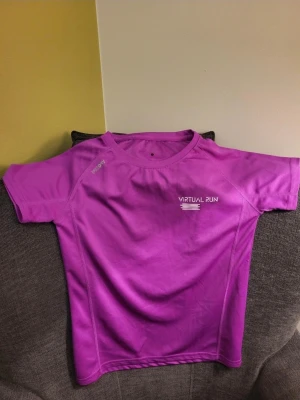 Lila tränings-tshirt från Blue Rebel M - Säljer en lila tränings-tshirt från Blue Rebel med tryck 'Virtual Run' och 'World Virtual Run' på ryggen. Tillverkad i 100% polyester, perfekt för löpning och sport. Snygg passform och korta ärmar, riktigt skön för aktiva dagar.