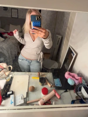 Beige omlottopp med knyt - Säljer en beige omlottopp med lång ärm och snygg v-ringning. Toppen har ett knyt i sidan som ger en cool och feminin look. Materialet känns mjukt och stretchigt, perfekt att styla med jeans eller kjol. Passformen är slim och toppen är enfärgad utan mönster.