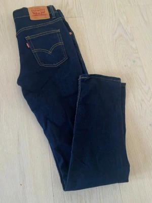 Levi's 512 mörkblå jeans - Snygga mörkblå Levi's 512 jeans med klassisk femficksdesign och kontrastsömmar. Jeansen har en slim passform och är tillverkade i mjukt jeansmaterial med en ikonisk läderpatch bak i midjan. Storlek 14A