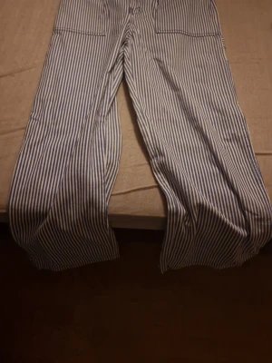 Randiga byxor från H&M Divided, strl 36 - Säljer ett par blåvit-randiga byxor från H&M Divided i storlek 36. Byxorna har raka ben, flera fickor och är tillverkade i bomull. Perfekta för dig som gillar en chill och stilren look med lite retrovibbar. Oanvända, prislapp saknas, inga deffekter. Priset kan diskuteras🫶