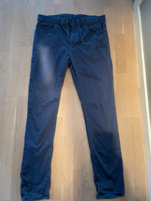 Mörkblå chinos uniqlo - Snygga mörkblå chinos med knytband i midjan och klassiska fickor fram. Byxorna har en rak passform och är tillverkade i mjukt bomullsmaterial som är skönt att bära hela dagen. Perfekta för dig som gillar en stilren och enkel look stl. 32/34