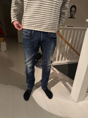 Replay blå jeans slim fit - Snygga Replay jeans i blå tvätt med slim fit och klassisk femficksdesign. Jeansen har dragkedja, knappstängning och coola slitningar på framsidan. 